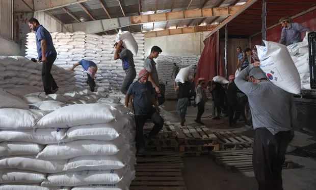 Workers unload bags of aid at a warehouse near the Syrian Bab al-Hawa